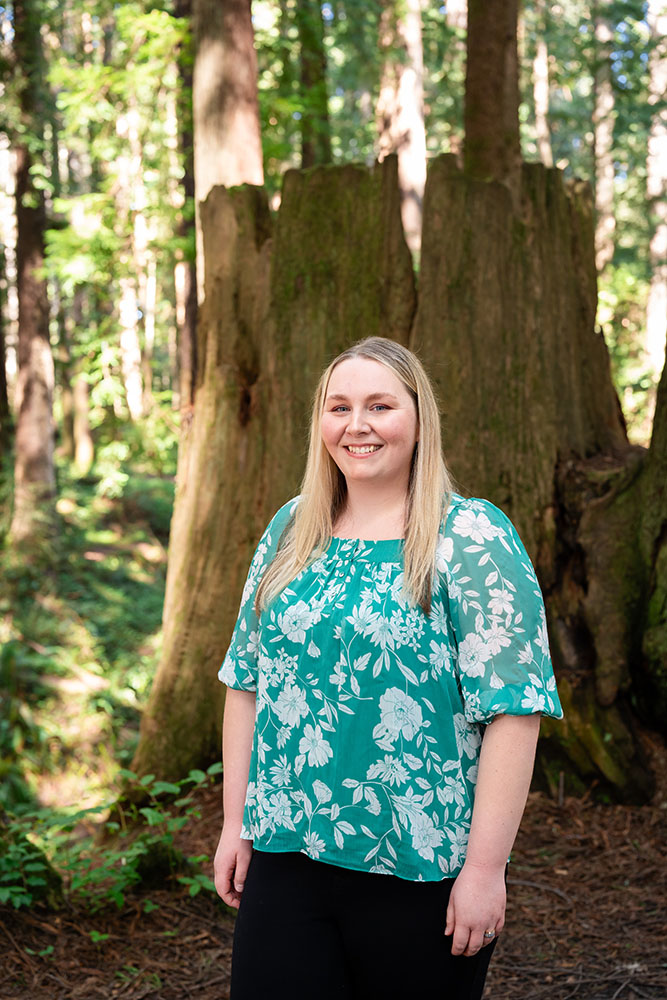 A well dressed woman stands in the forest and smiles