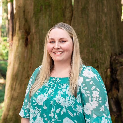 A well dressed woman stands in the forest and smiles