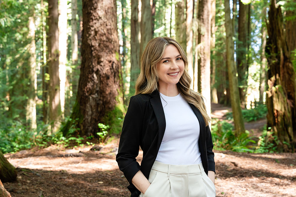 A well dressed woman stands in the forest and smiles