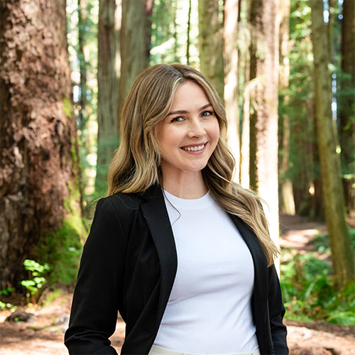 A well dressed woman stands in the forest and smiles