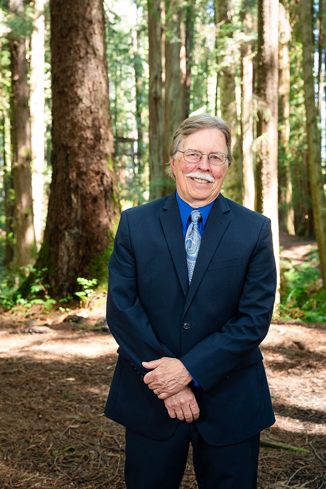 A well dressed man stands in the forest and smiles