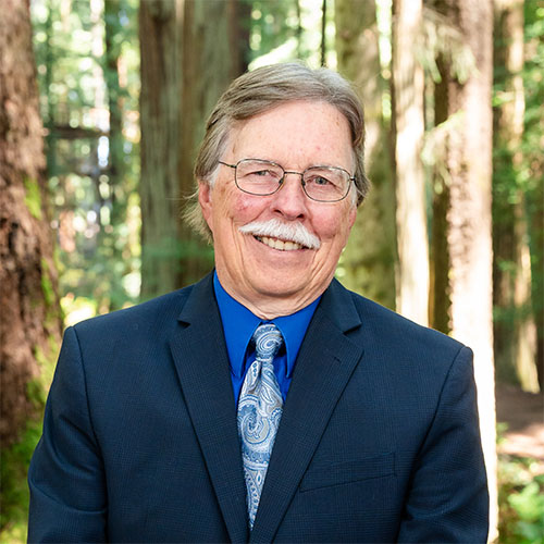 A well dressed man stands in the forest and smiles