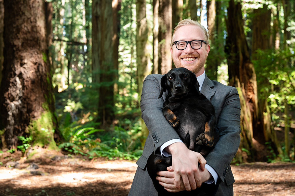A well dressed man stands in the forest and smiles