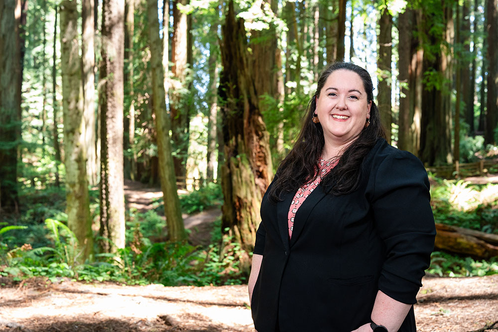 A well dressed woman stands in the forest and smiles