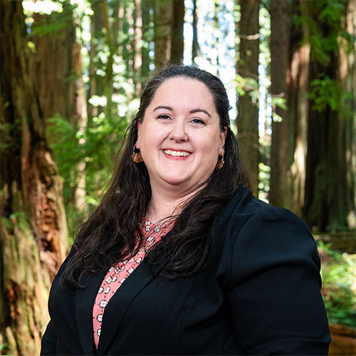 A well dressed woman stands in the forest and smiles