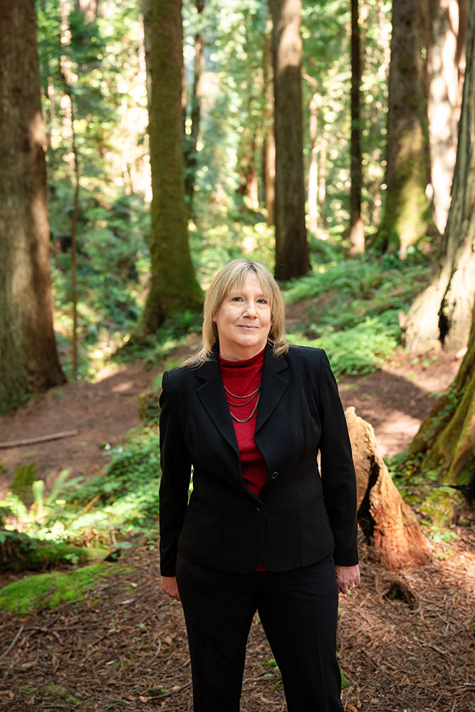 A well dressed woman stands in the forest and smiles
