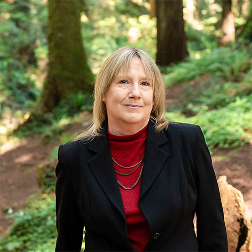 A well dressed woman stands in the forest and smiles