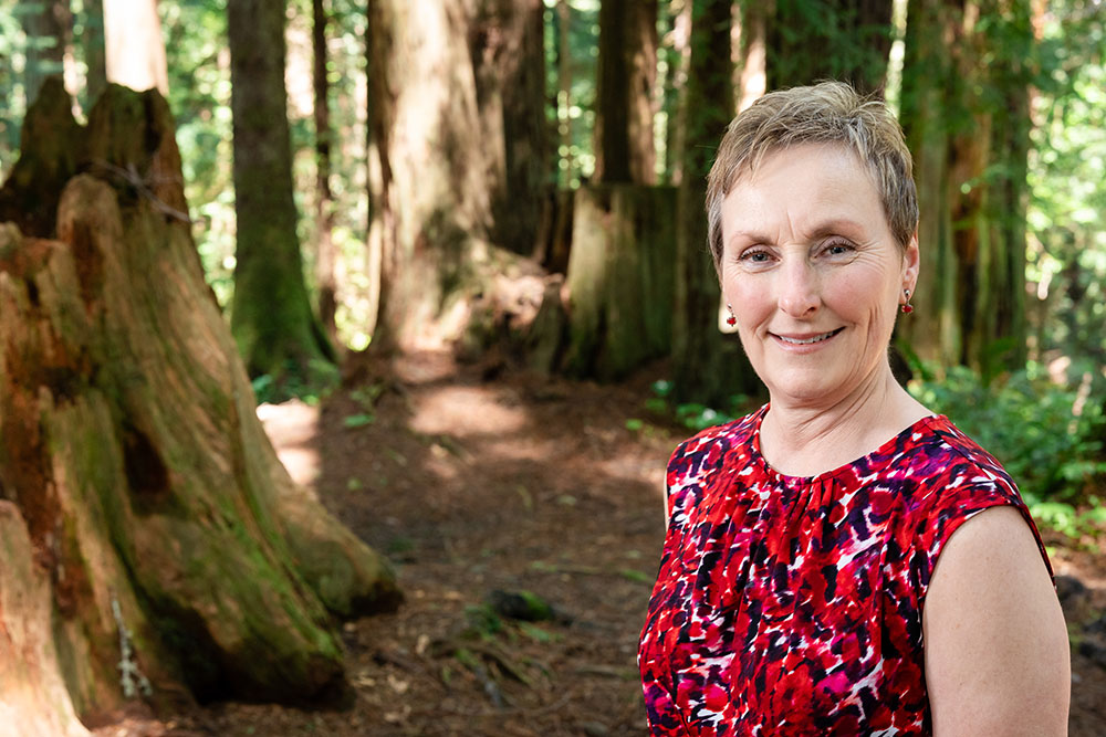 A well dressed woman stands in the forest and smiles