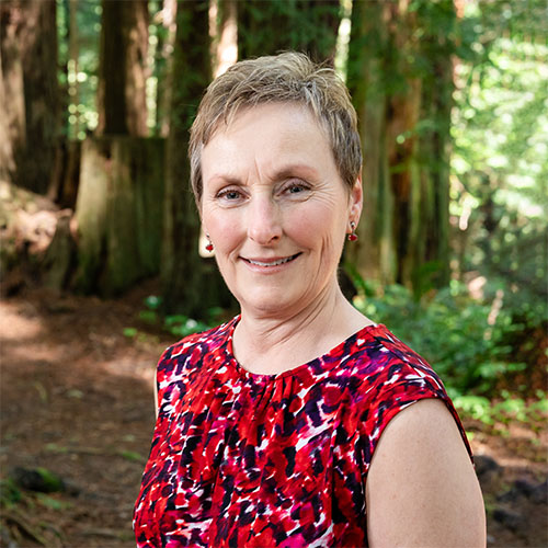 A well dressed woman stands in the forest and smiles