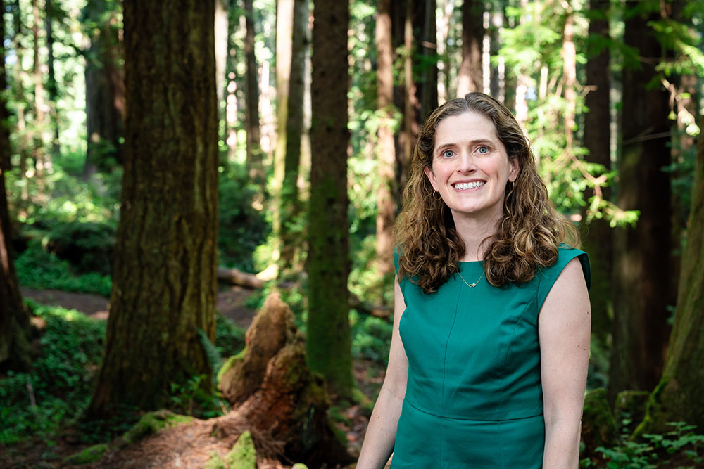 A well dressed woman stands in the forest and smiles