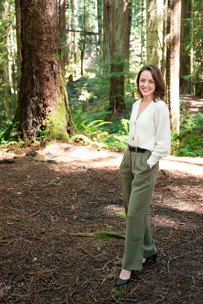 A well dressed woman stands in the forest and smiles