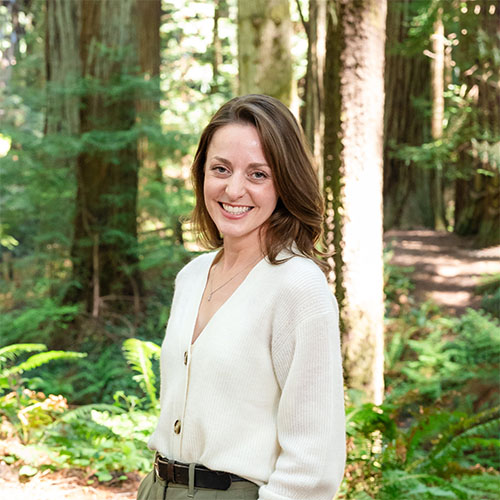 A well dressed woman stands in the forest and smiles