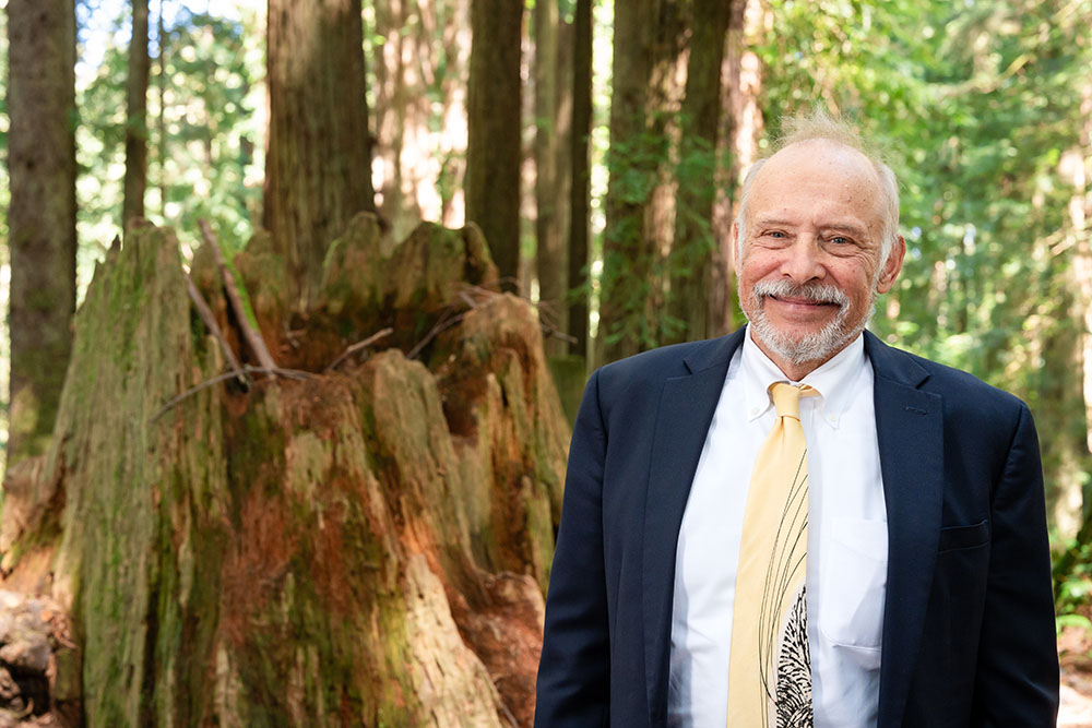A well dressed man stands in the forest and smiles