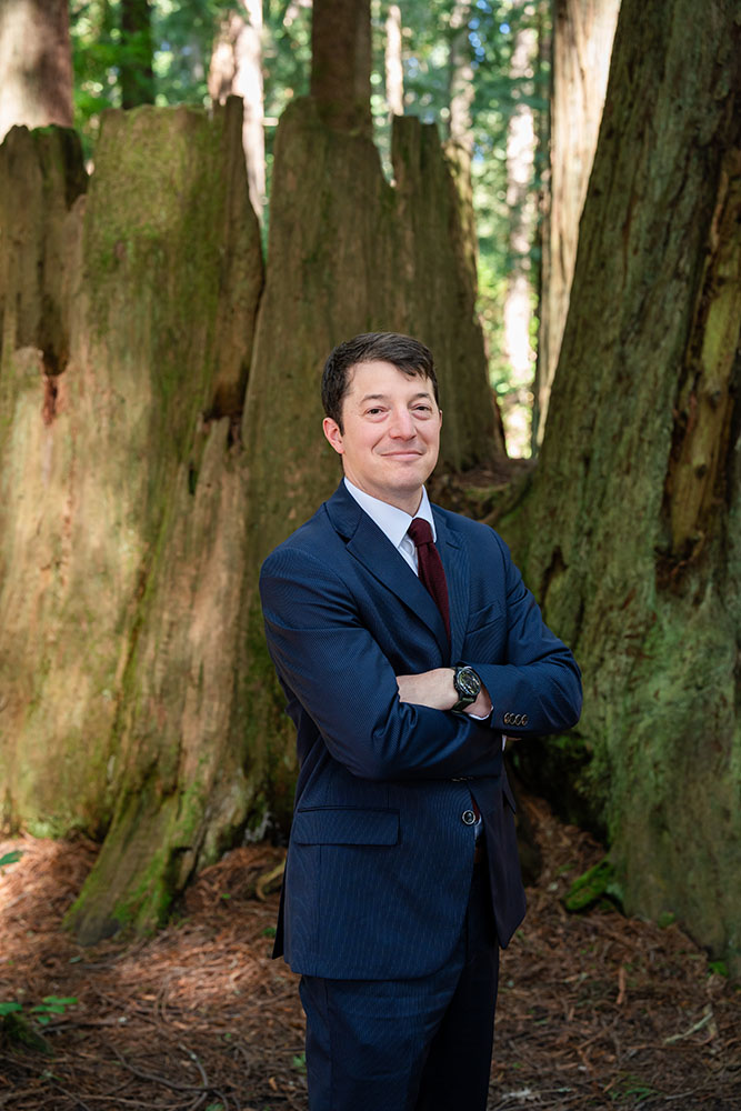 A well dressed man stands in the forest and smiles