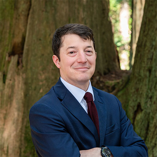 A well dressed man stands in the forest and smiles